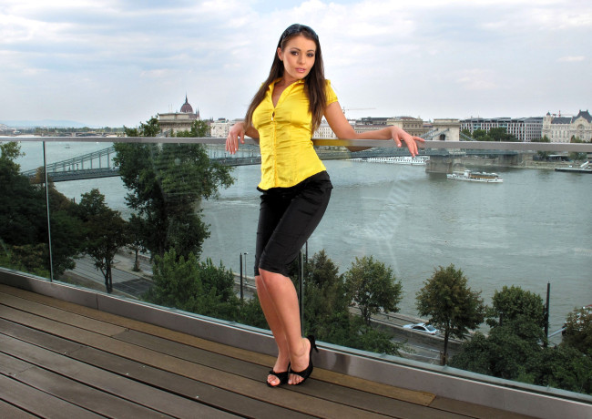 Обои картинки фото девушки, nelly sullivan , stella moran, шатенка, топ, бриджи, каблуки, балкон, панорама, город, дома, мост, река