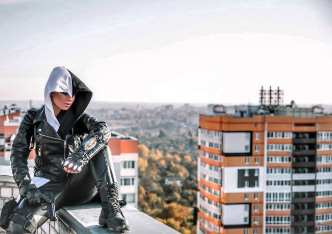 Обои картинки фото девушки, анна шаховская, образ, косплей, наряд, костюм, капюшон, косуха, оружие, крыши, дома, город, панорама