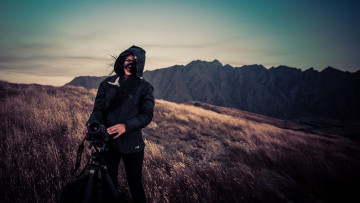 Картинка девушки -unsort+ брюнетки +шатенки горы камера фотоаппарат куртка улыбка трава ветер брюнетка