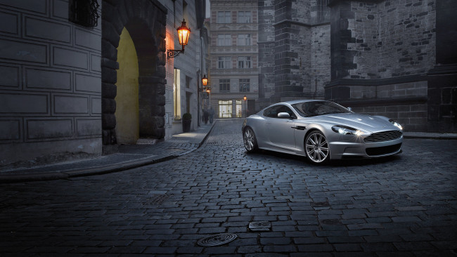 Обои картинки фото автомобили, aston martin, серебристый, город, улица, арка, дома