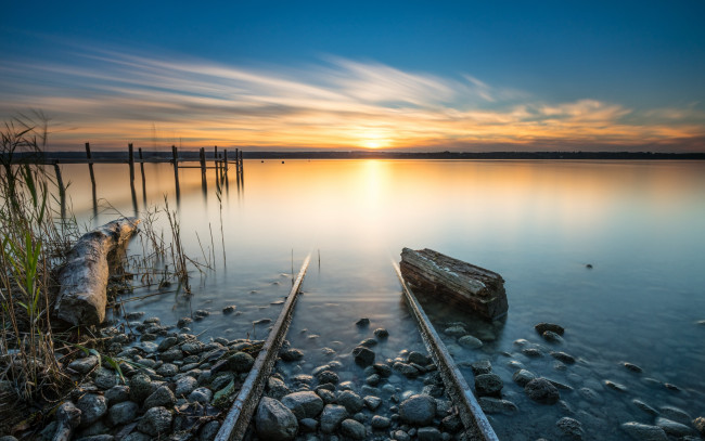 Обои картинки фото природа, реки, озера, камни, утро, спокойствие, бревно, берег, сваи, путь, в, никуда, солнце, горизонт, рельсы, облака, водоем, озеро, рассвет, небо, трава, пейзаж