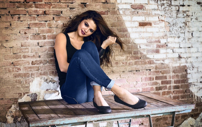 Обои картинки фото девушки, selena gomez, шатенка, майка, джинсы, скамейка, стена